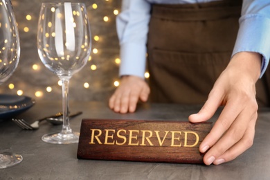 Photo of Waiter setting RESERVED sign on restaurant table, closeup