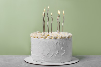 Photo of Delicious cake with cream and burning candles on grey table