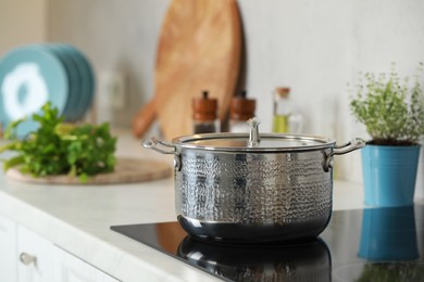 Pot with lid on cooktop in kitchen, space for text. Cooking utensils