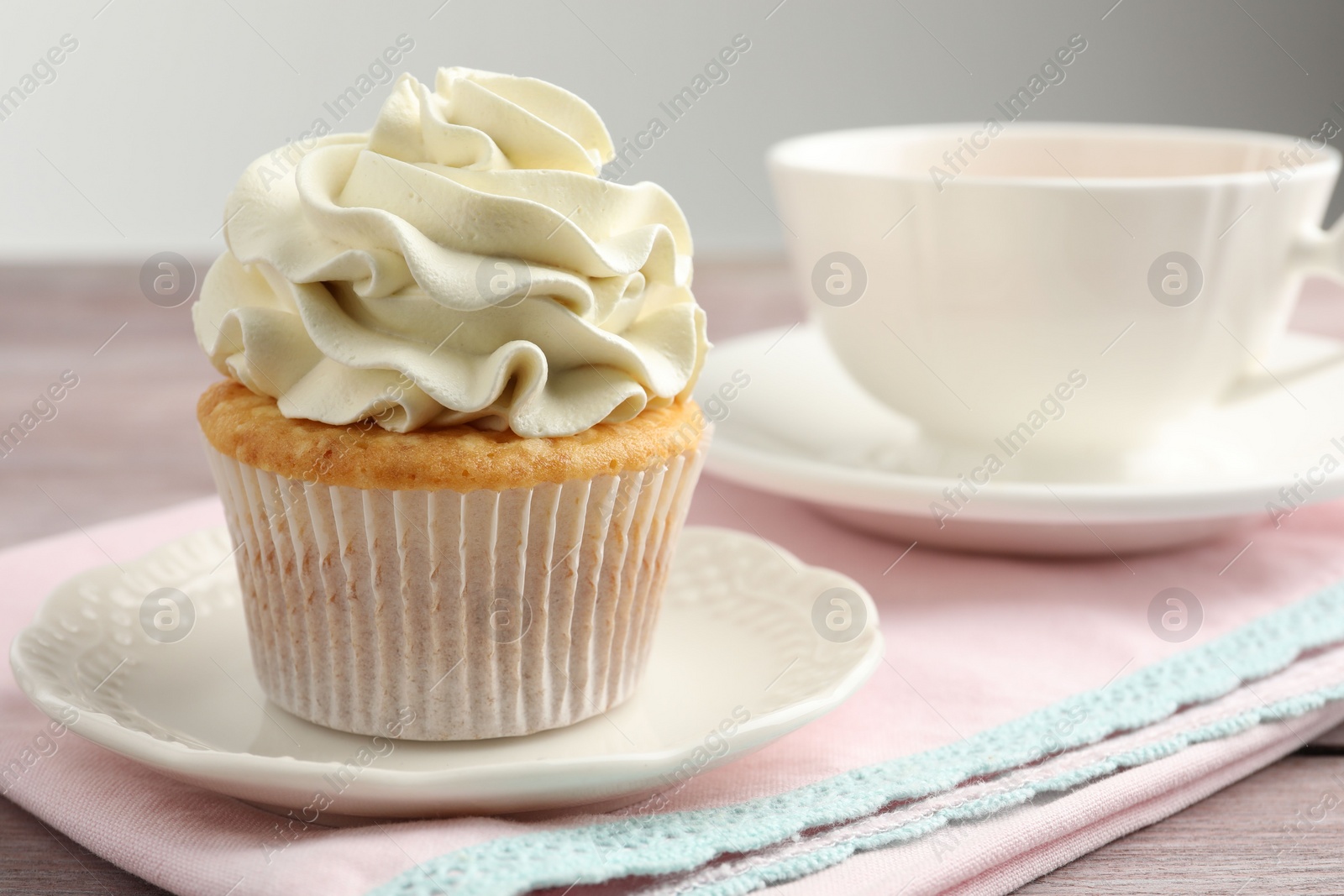 Photo of Tasty cupcake with vanilla cream on pink wooden table, closeup