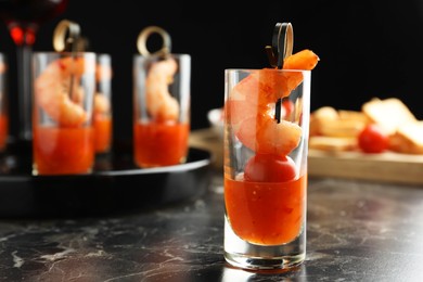 Photo of Tasty canape with shrimp, tomato and sauce in shot glass on black marble table, closeup. Space for text