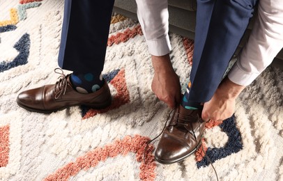 Man with colorful socks putting on stylish shoes indoors, closeup