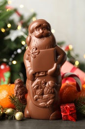 Composition with chocolate Santa Claus candies on grey table near Christmas tree, closeup