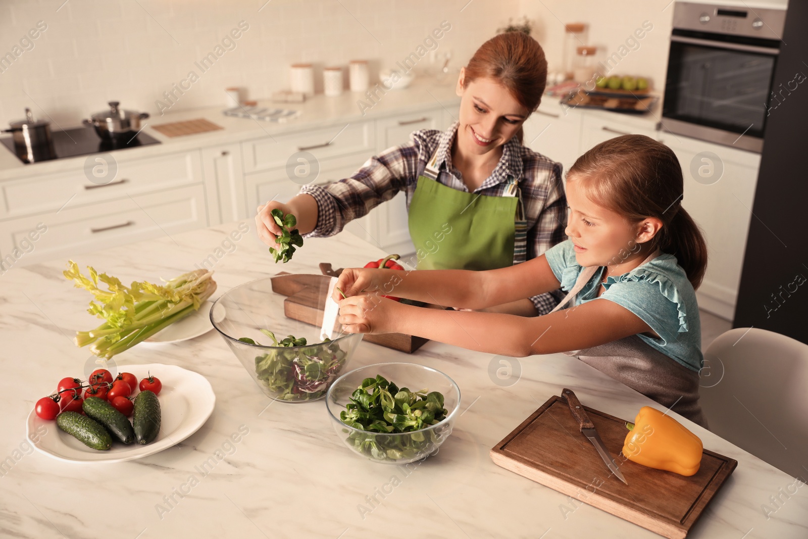 Photo of Mother and daughter cooking salad together in kitchen