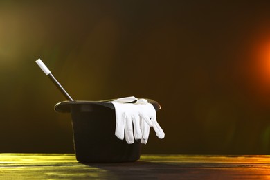 Photo of Magician's hat, wand and gloves on wooden table against lamps and dark background, space for text