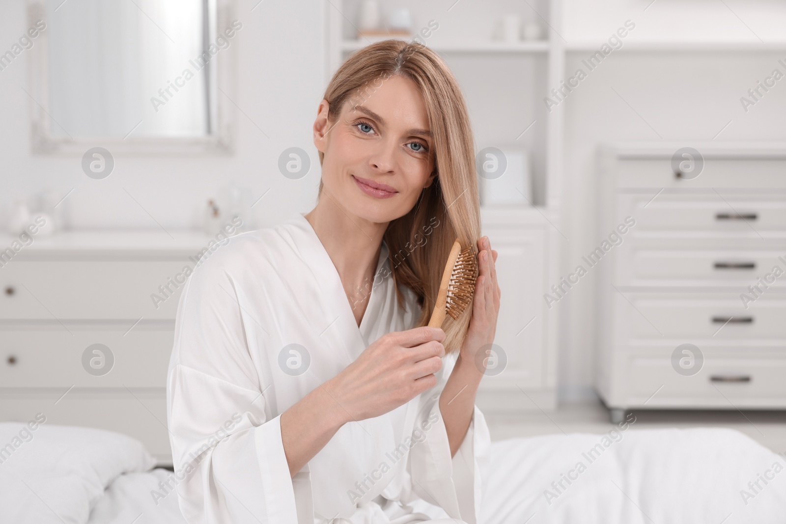 Photo of Beautiful woman brushing her hair on bed in room