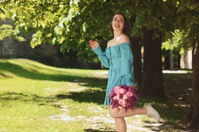 Beautiful woman with bouquet of spring flowers in park on sunny day, space for text