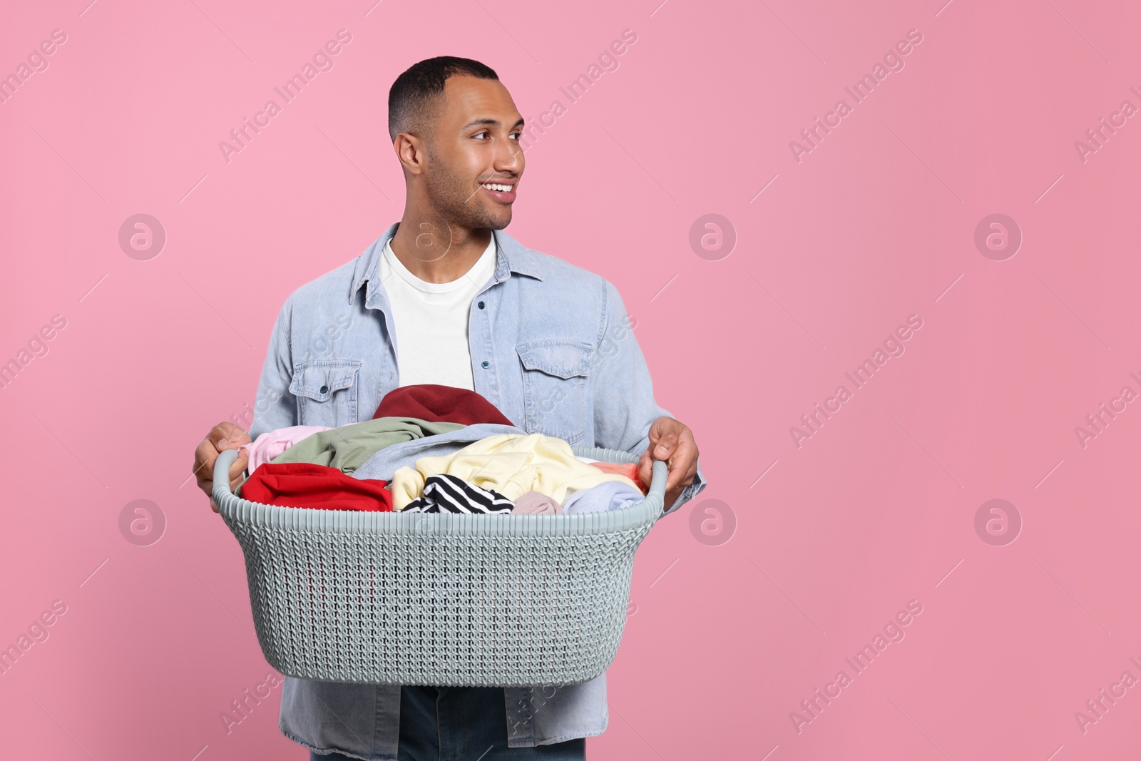 Photo of Happy man with basket full of laundry on pink background. Space for text