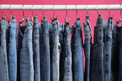 Rack with stylish jeans on pink background, closeup