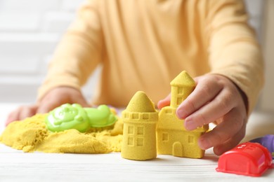 Photo of Little child playing with yellow kinetic sand at white wooden table, closeup