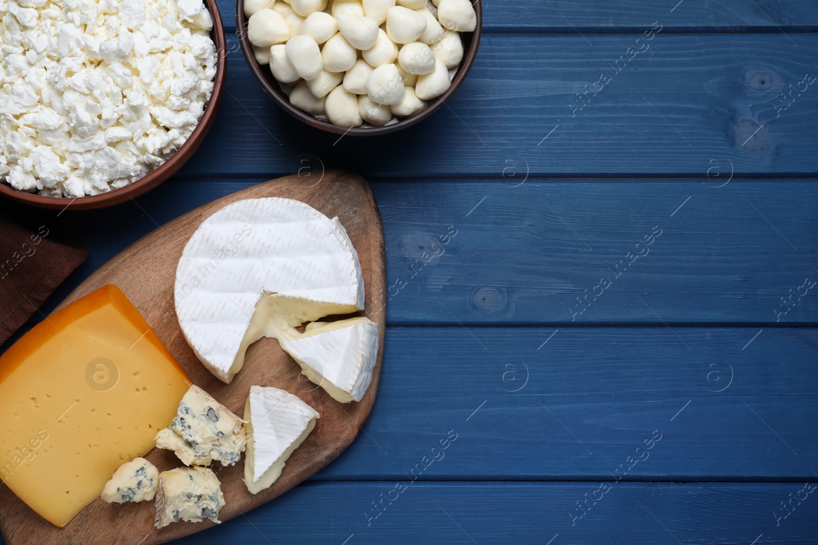 Photo of Clay dishware with fresh dairy products on blue wooden table, flat lay. Space for text