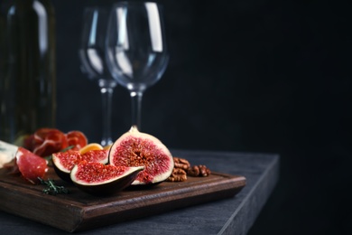 Photo of Wooden board with ripe fig slices on table against dark background. Space for text