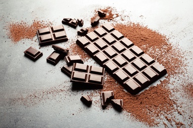 Pieces of chocolate and cocoa powder on grey background