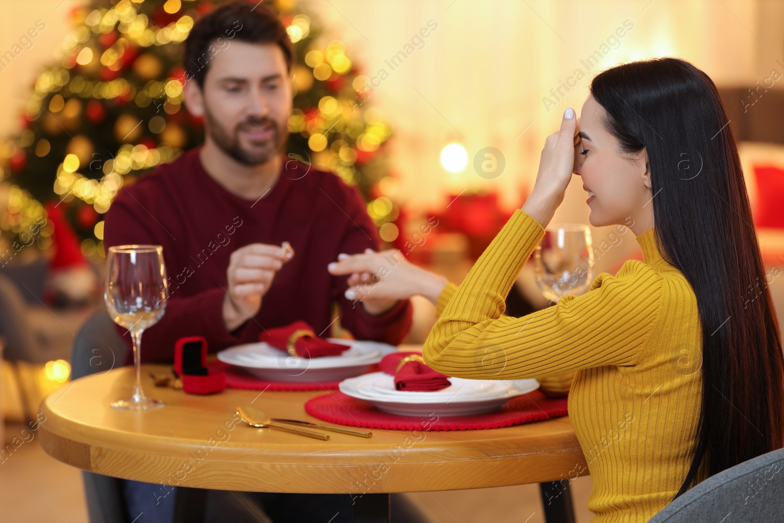 Photo of Making proposal. Man putting engagement ring on his girlfriend's finger at home on Christmas, selective focus