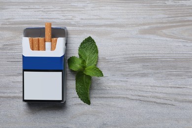 Pack of menthol cigarettes and mint on light wooden table, flat lay. Space for text
