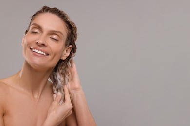 Photo of Portrait of beautiful happy woman washing hair on light grey background. Space for text