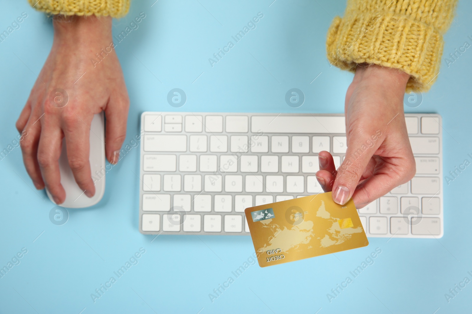 Photo of Online payment. Woman using credit card and computer at light blue table, top view