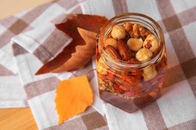 Photo of Different nuts with honey in jar and dry leaves on wooden table, above view. Space for text