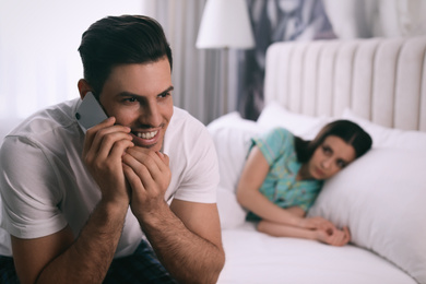 Photo of Man preferring talking on phone over spending time with his girlfriend at home. Jealousy in relationship