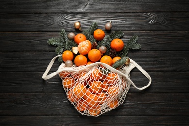 Photo of Flat lay Christmas composition with fresh tangerines in mesh bag on dark wooden table