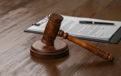 Photo of Wooden gavel near clipboard with documents on table. Law and justice