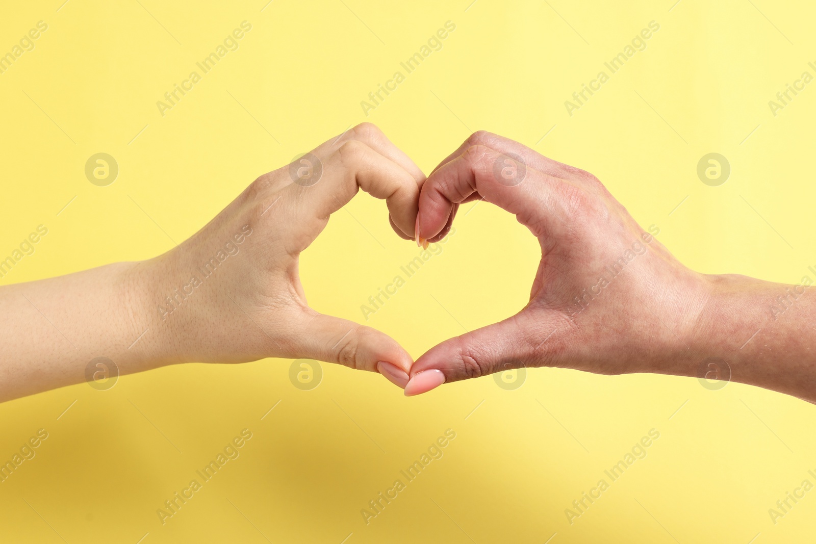 Photo of Woman showing heart gesture with hands on yellow background, closeup