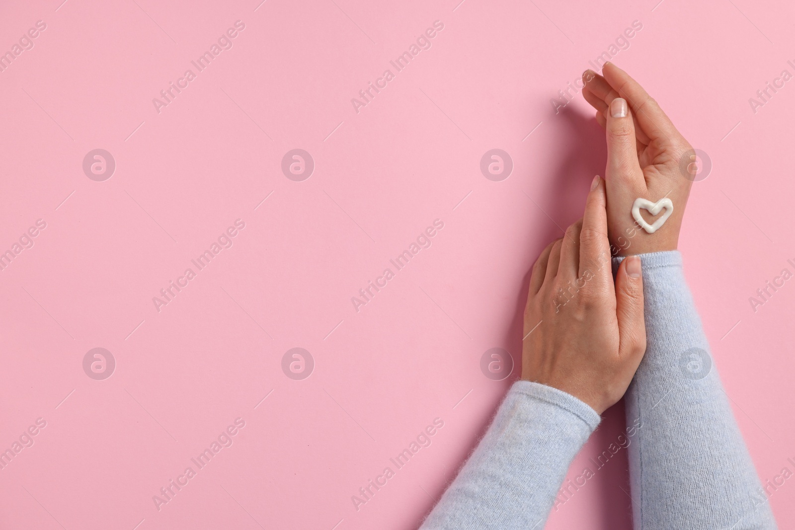 Photo of Woman with heart made of cosmetic cream on hand against pink background, top view. Space for text