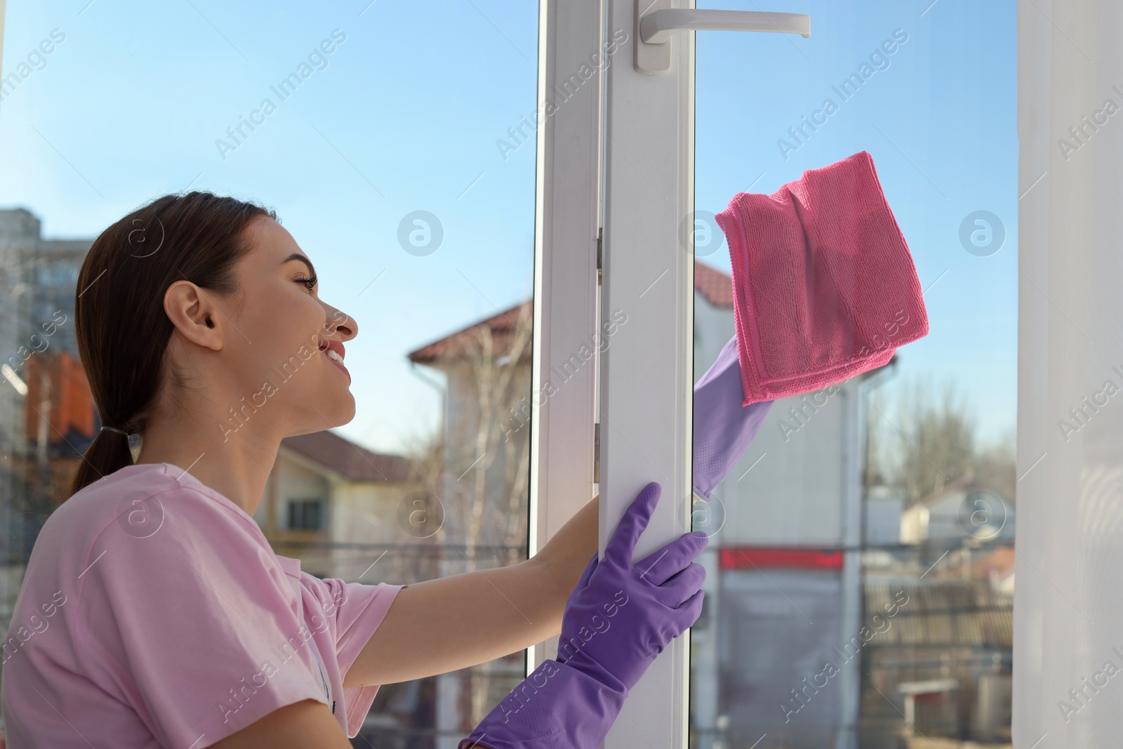 Photo of Young woman cleaning window glass with rag at home