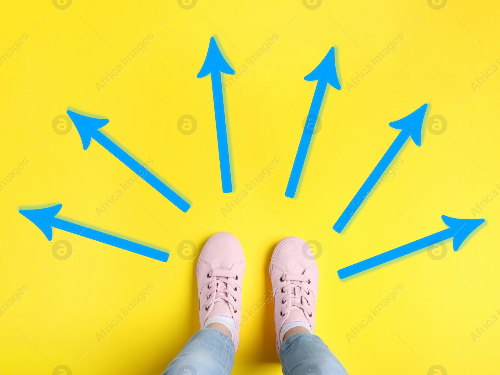 Image of Choosing future profession. Girl standing in front of drawn signs on yellow background, top view. Arrows pointing in different directions symbolizing diversity of opportunities