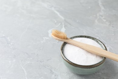 Bamboo toothbrush and bowl of baking soda on light gray marble table, space for text