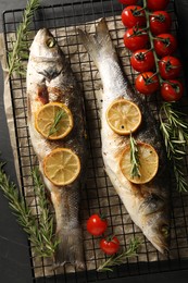 Photo of Baked fish with tomatoes, rosemary and lemon on black table, top view