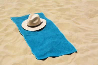 Photo of Soft blue towel and straw hat on sandy beach, space for text