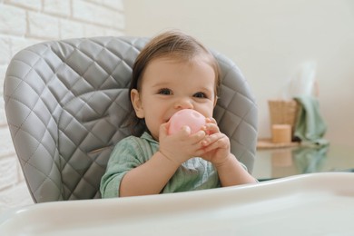 Photo of Cute little baby nibbling toy in high chair indoors