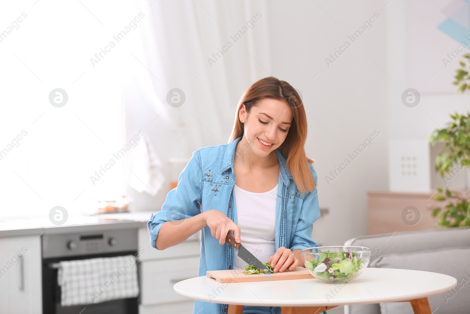 Photo of Happy young woman preparing salad in kitchen. Healthy diet