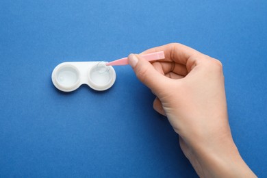 Photo of Woman taking contact lens from case with tweezers on blue background, top view