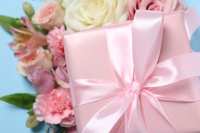 Photo of Gift box and beautiful flowers on light blue background, closeup