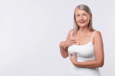 Photo of Beautiful senior woman doing breast self-examination on white background, space for text