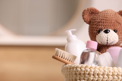 Photo of Baby cosmetic products, bath accessories and toy bear in knitted basket indoors, closeup. Space for text