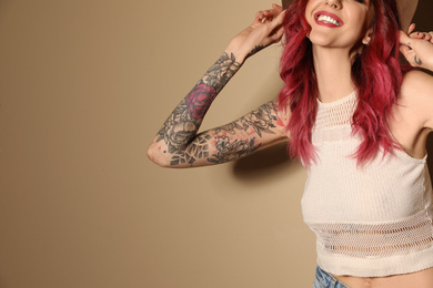 Beautiful woman with tattoos on arms against beige background, closeup. Space for text