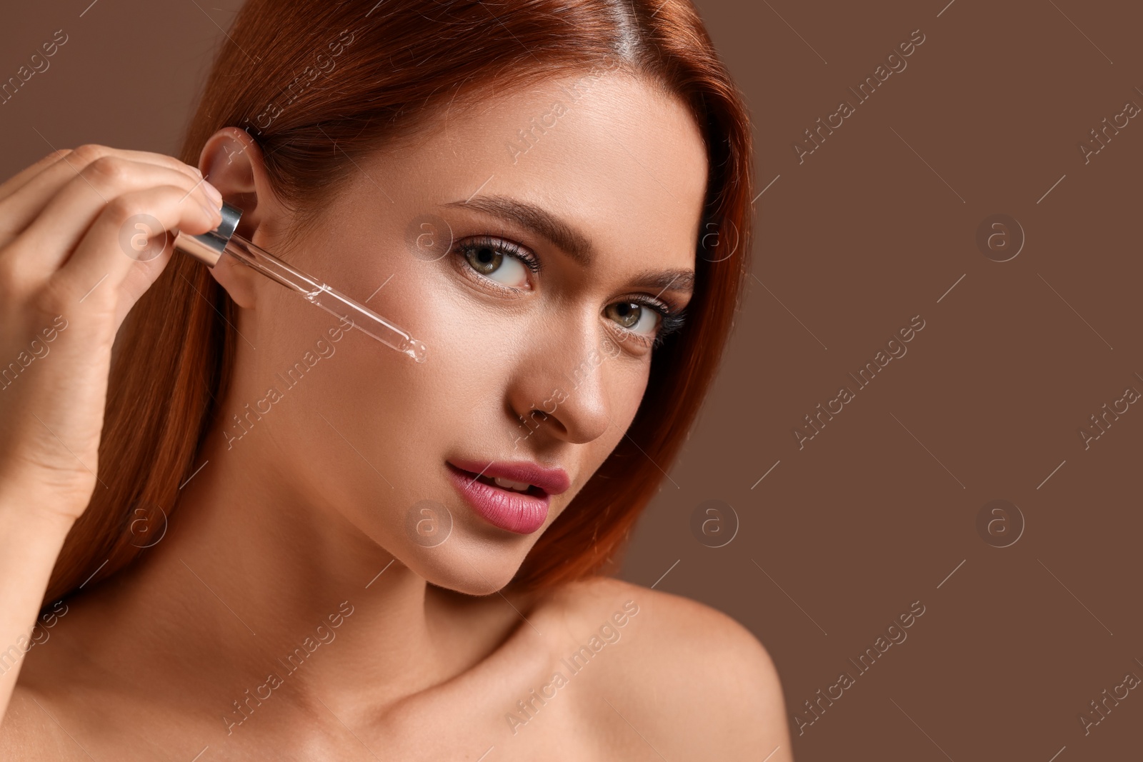 Photo of Beautiful young woman applying cosmetic serum onto her face on brown background, closeup. Space for text