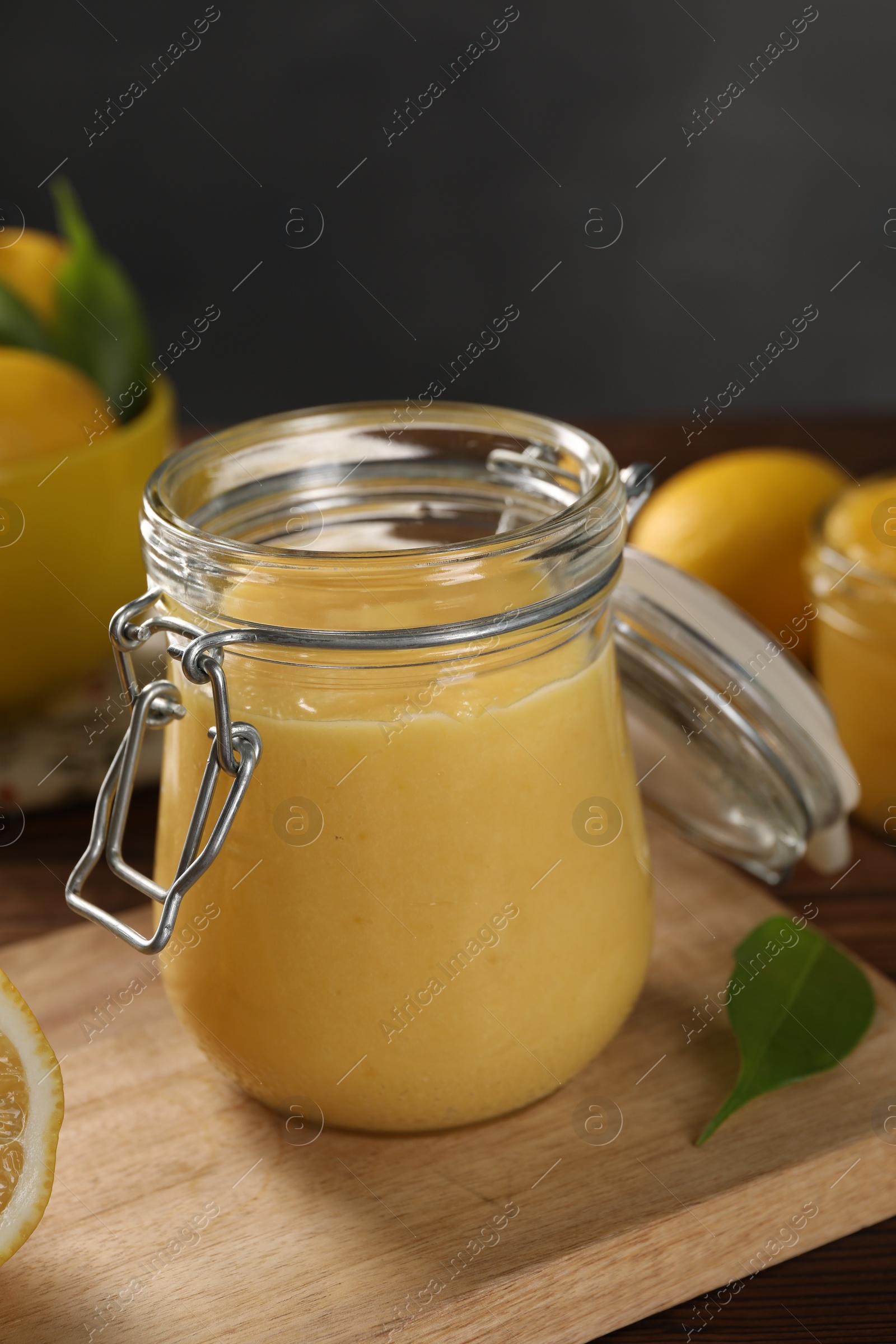 Photo of Delicious lemon curd in glass jar and green leaf on table
