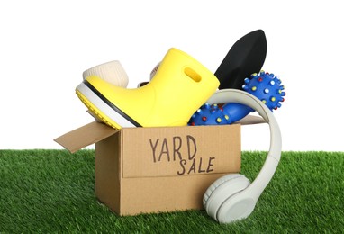 Photo of Phrase Yard Sale written on box with different stuff on green grass against white background