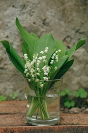 Photo of Beautiful lily of the valley flowers in glass vase on stone parapet outdoors