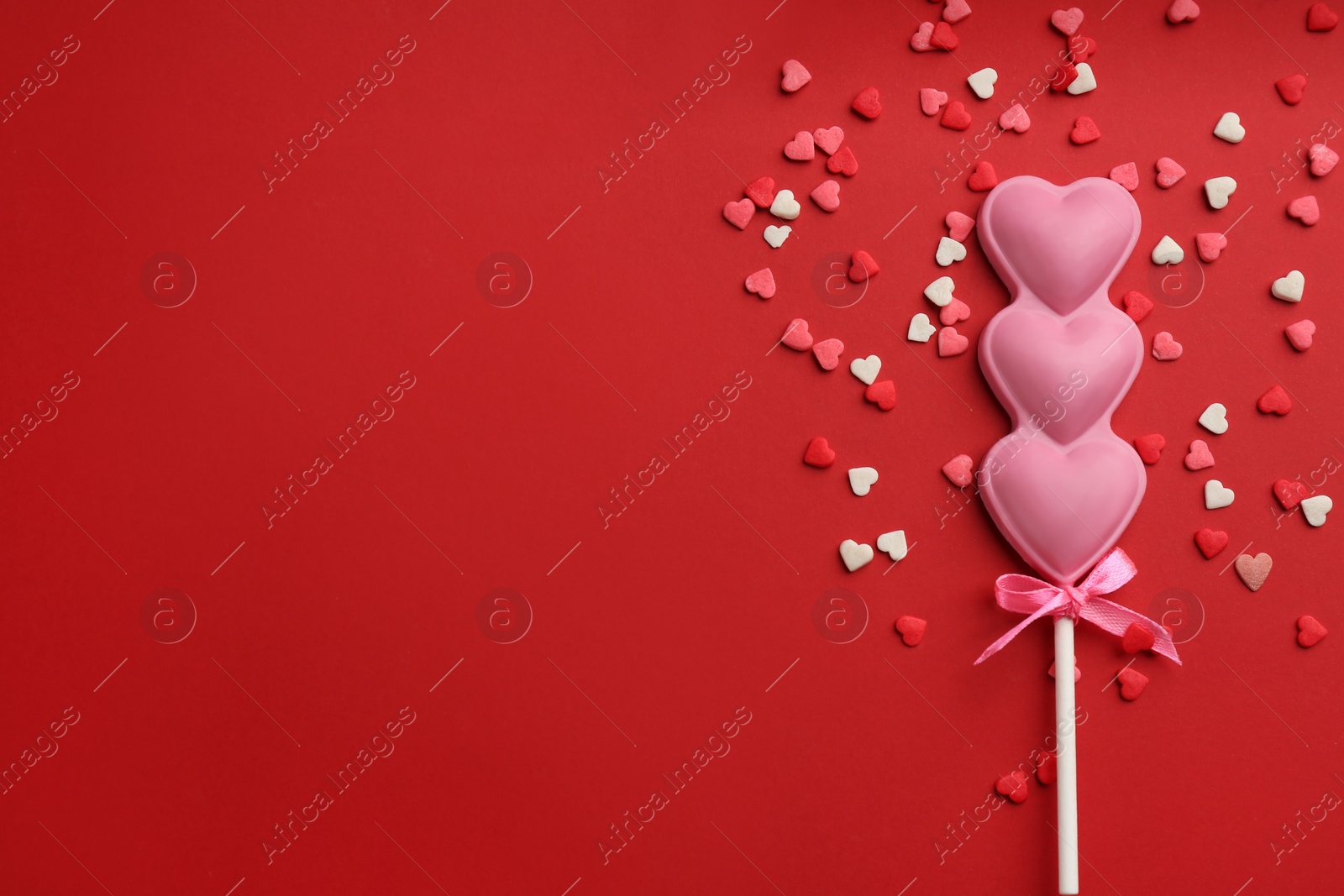 Photo of Chocolate heart shaped lollipop and sprinkles on red background, flat lay. Space for text