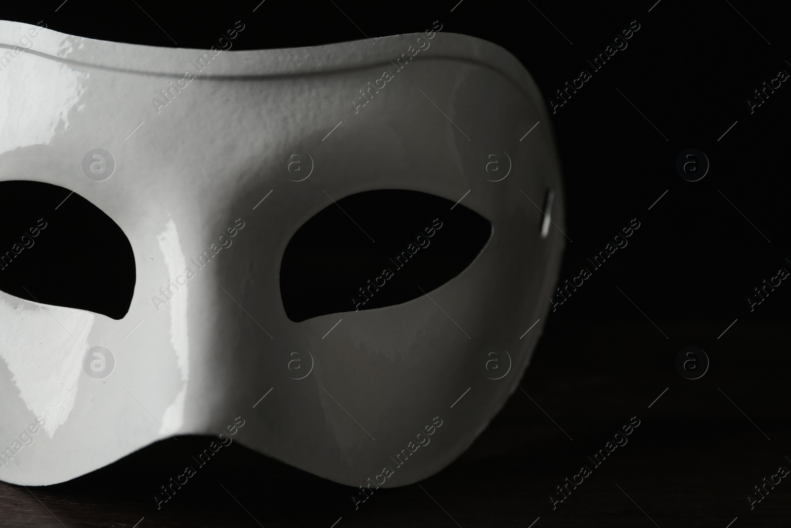 Photo of White theatre mask on table against black background, closeup