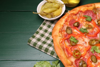 Photo of Delicious pizza Diablo, pickled peppers and parsley on green wooden table, closeup. Space for text