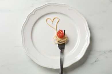 Photo of Heart made of tasty spaghetti, fork and tomato on white marble table, top view