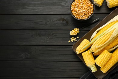 Photo of Tasty fresh corn cobs and kernels on black wooden table, flat lay. Space for text