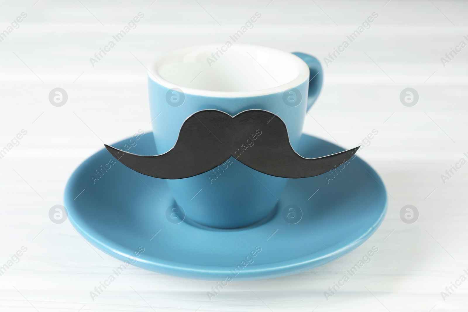 Photo of Cup with fake paper mustache and saucer on white table