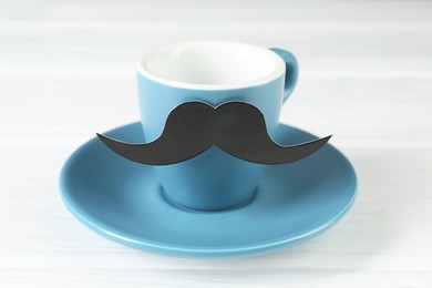Cup with fake paper mustache and saucer on white table
